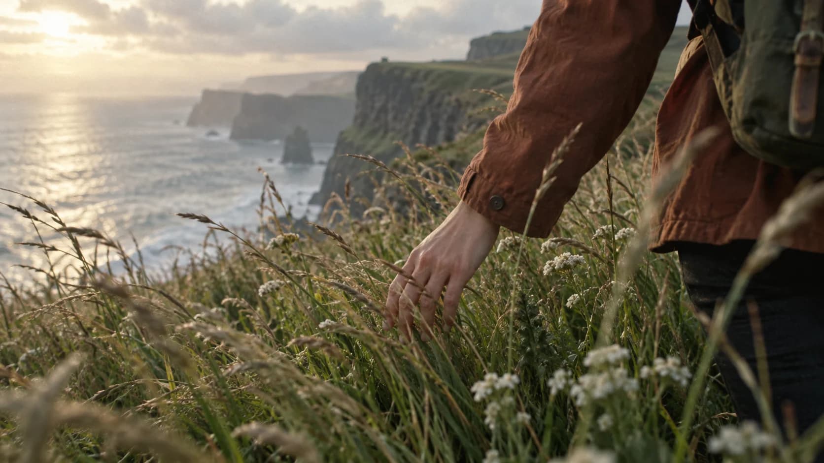 A traveler's hand brushing through coastal grasses